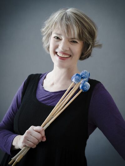 Person with short hair, wearing a purple and black dress, holding percussion mallets.