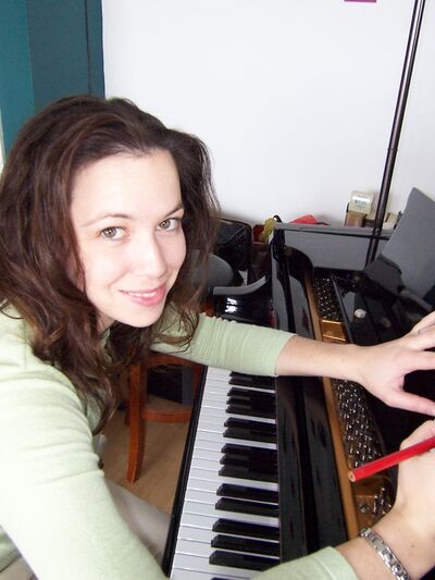 Person wearing a green shirt, smiling and looking at the camera while composing music on a grand piano.
