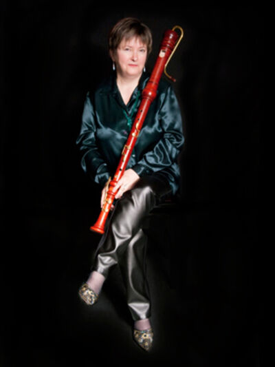 Person sitting with their legs crossed, wearing dark-colored satin, holding a bassoon.