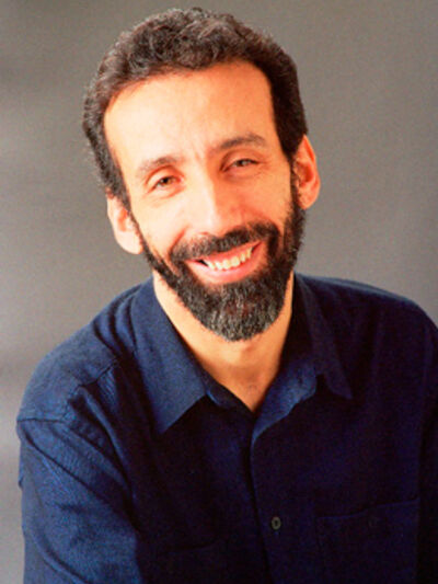 Headshot of a person with a beard, wearing a navy button-down shirt in front of a grey background.