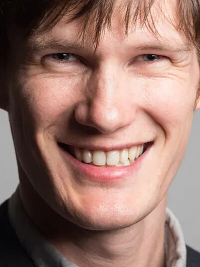 headshot of person with blue eyes, wearing a suit, smiling warmly.