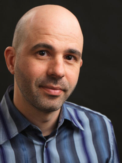 Bald person wearing a blue striped shirt, looking at the camera with a dark background, creating a focused and confident look.