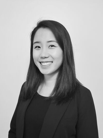 Black and white headshot of a person wearing all black, including a blazer, smiling confidently.