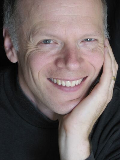 Person wearing a black shirt, smiling and gently holding their face, creating a warm and approachable expression.