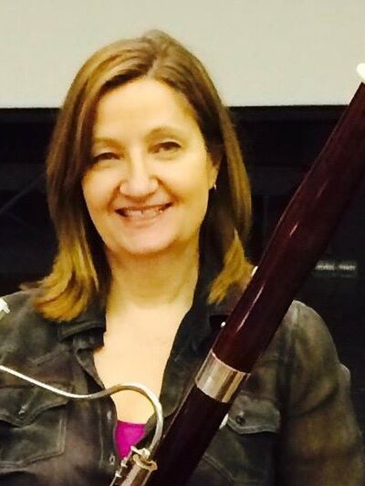 Person wearing a button-up shirt, smiling while holding a bassoon.