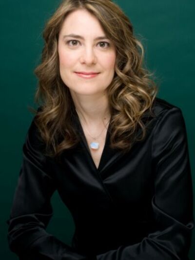 Headshot of a person smiling, wearing a black satin shirt, with a green background that adds vibrancy.