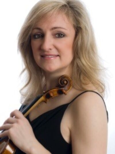 A headshot of a person with shoulder-length blonde hair, wearing a black tank top and holding a violin, set against a white background.