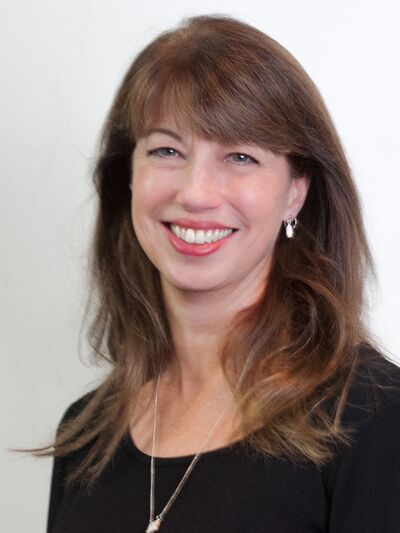 Headshot of a person with shoulder-length hair and bangs, smiling while wearing a black shirt