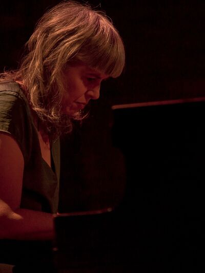 Person with bangs wearing a green shirt playing the piano, focused and concentrated.
