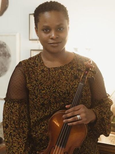 A person wearing a black patterned blouse is holding a violin.