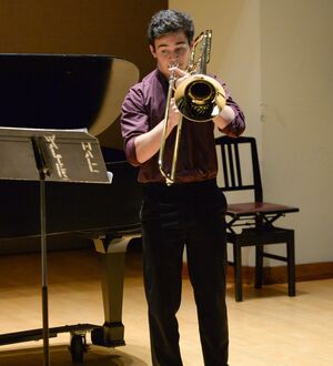 Person playing the trombone as a soloist onstage, wearing dress clothes, with a focused expression.