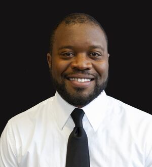 Man wearing a shirt and tie, smiling, with a dark background.