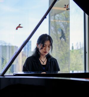 Yuchen Zhang plays piano in one of the Faculty of Music's classrooms/practice rooms (with a view of the U of T campus and Toronto cityscape outside of the window behind her).