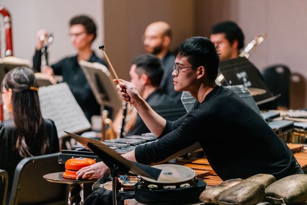 Percussionist wearing black in an ensemble, holding a mallet in hand and ready to play a bell.