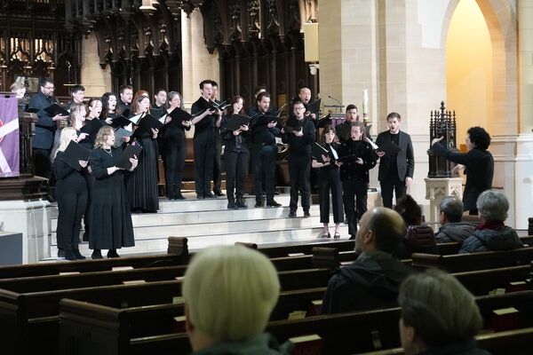 Choir in performance attire singing in a chapel, captured from the audience's perspective, with the chapel's architecture and warm lighting enhancing the atmosphere.