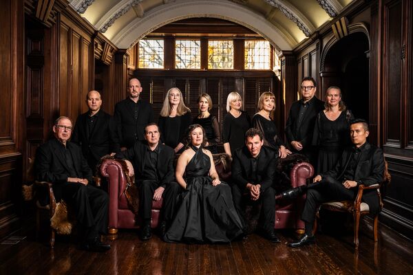 Posed group photo of individuals in performance attire standing in a hallway, featuring elegant architectural details and a vintage atmosphere.