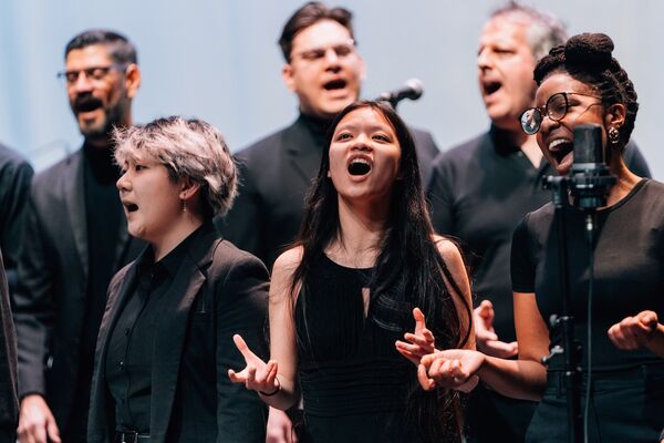 Choir performing on stage in performance attire, emotionally singing into microphones, with expressions of passion and focus.