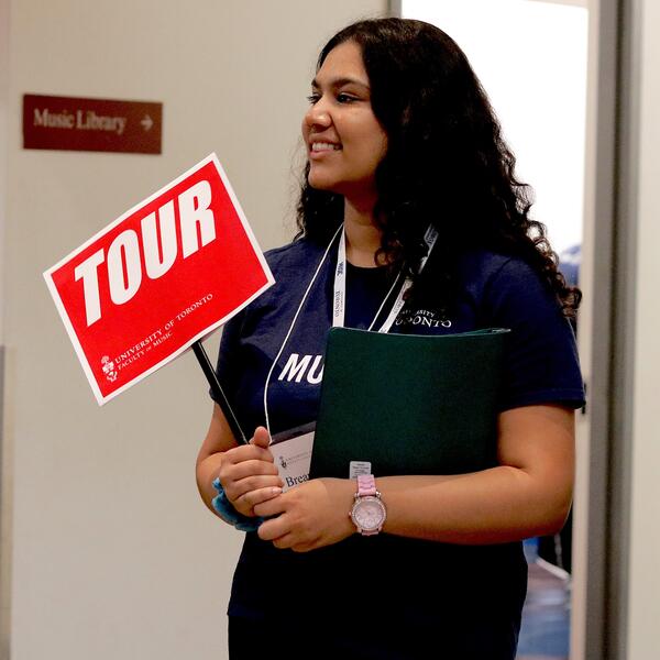 A U of T Music Student Ambassador holds a Tour sign.