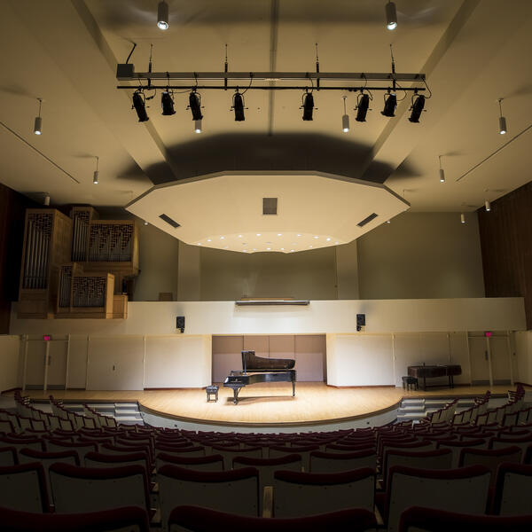 Empty performance hall with a grand piano placed on the stage, highlighting the spaciousness of the venue.